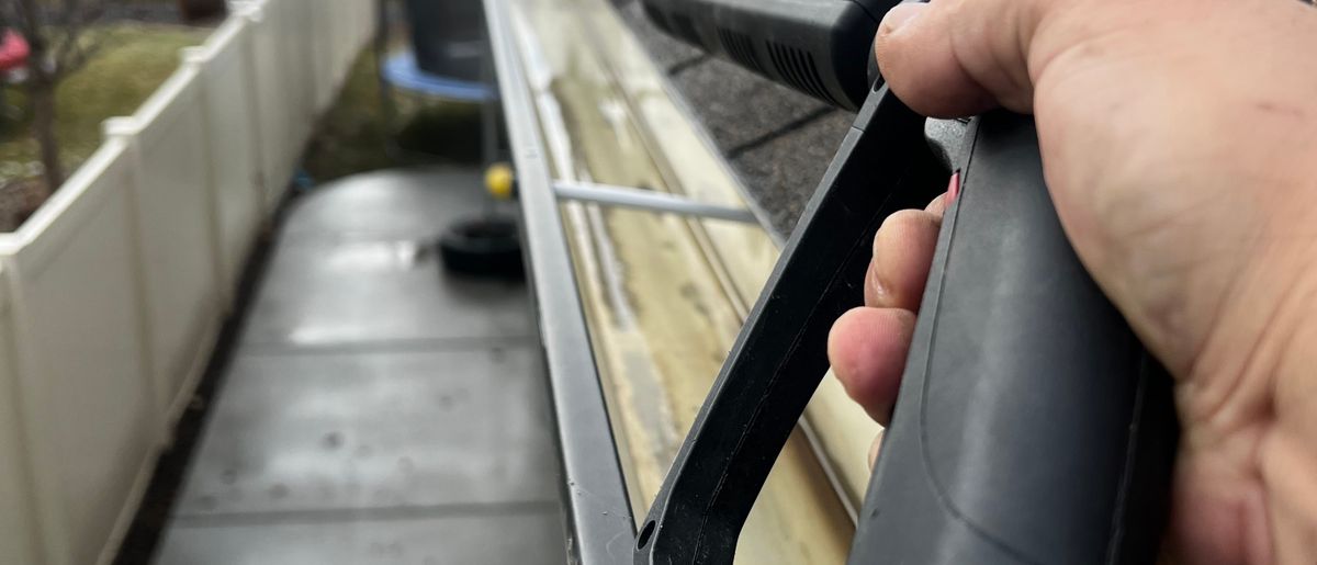 Gloved hands scooping leaves out of a gutter