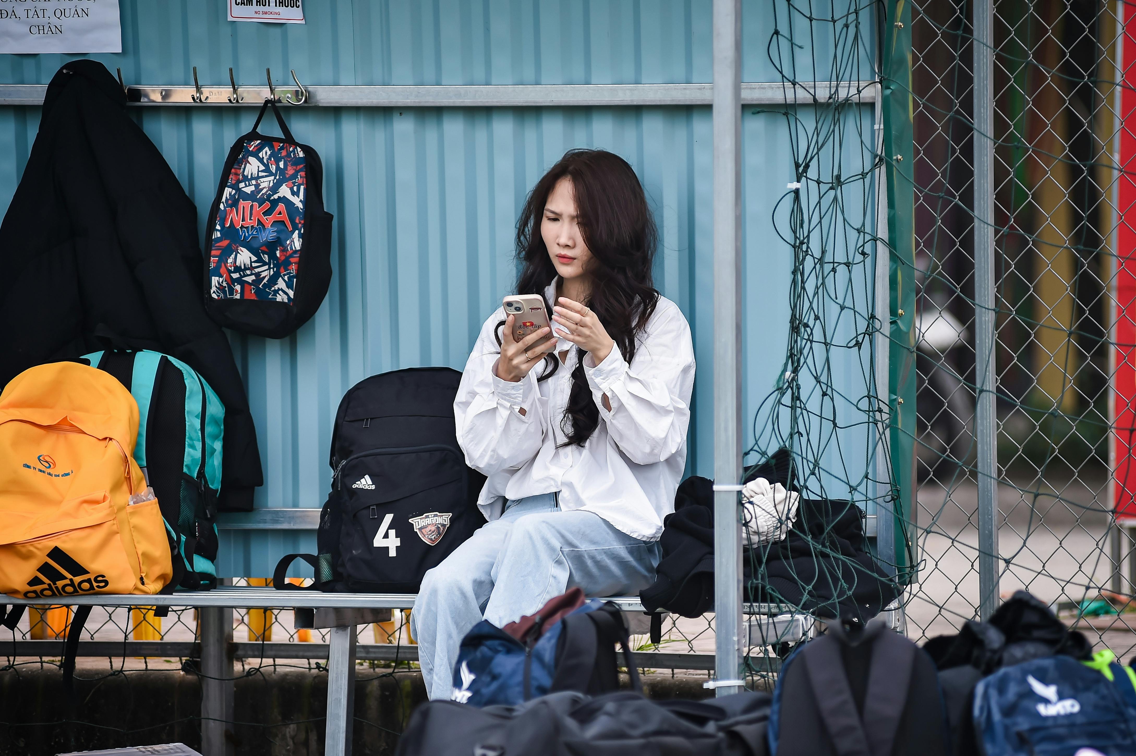 Young woman on a bench with backpacks, focused on her phone outdoors.