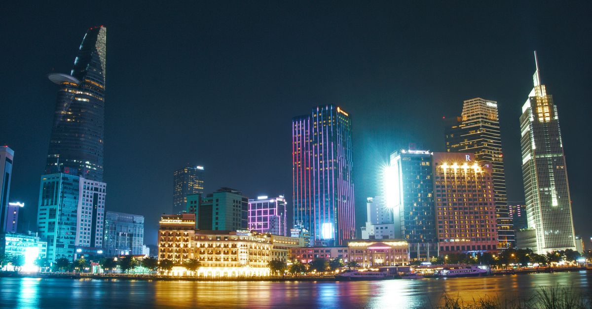 Illuminated skyscrapers reflecting on water in Ho Chi Minh City at night, showcasing urban beauty.