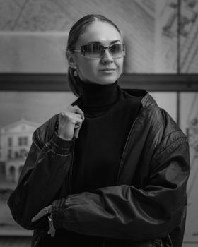 Elegant woman in a black leather jacket and sunglasses looks confident indoors.