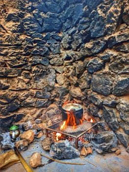 Stone-walled outdoor cooking scene with pot on open fire.