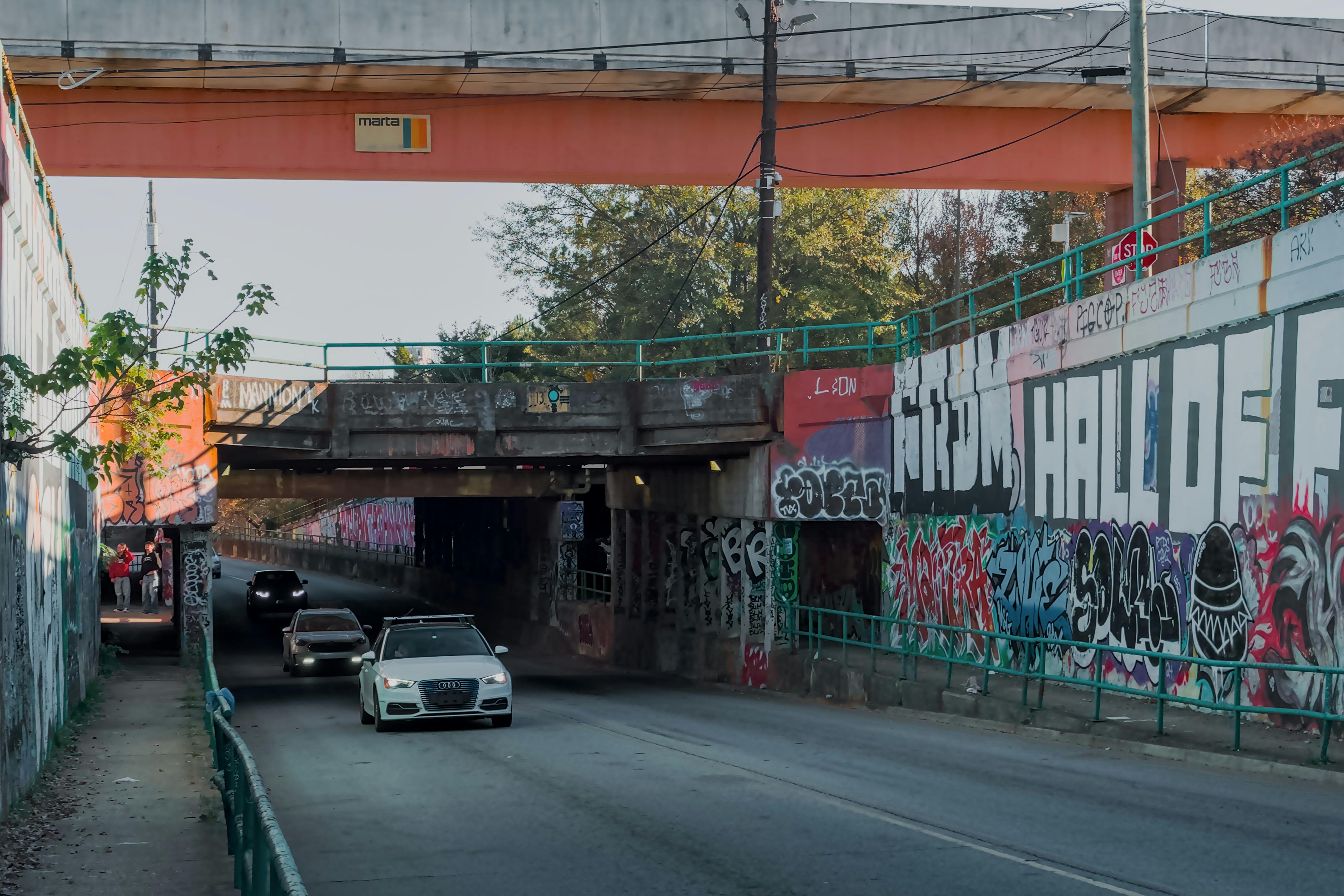 Colorful graffiti on an urban underpass in Atlanta with cars passing through.