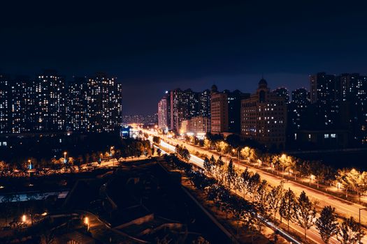 Nighttime view of a cityscape with illuminated buildings and traffic light trails.