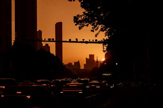 Silhouette of city skyline at sunset with bustling traffic below, warm lighting.