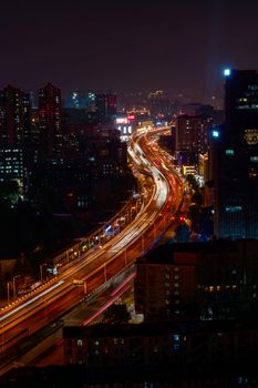 Dramatic cityscape at night with vibrant light trails on a highway, showcasing urban life.