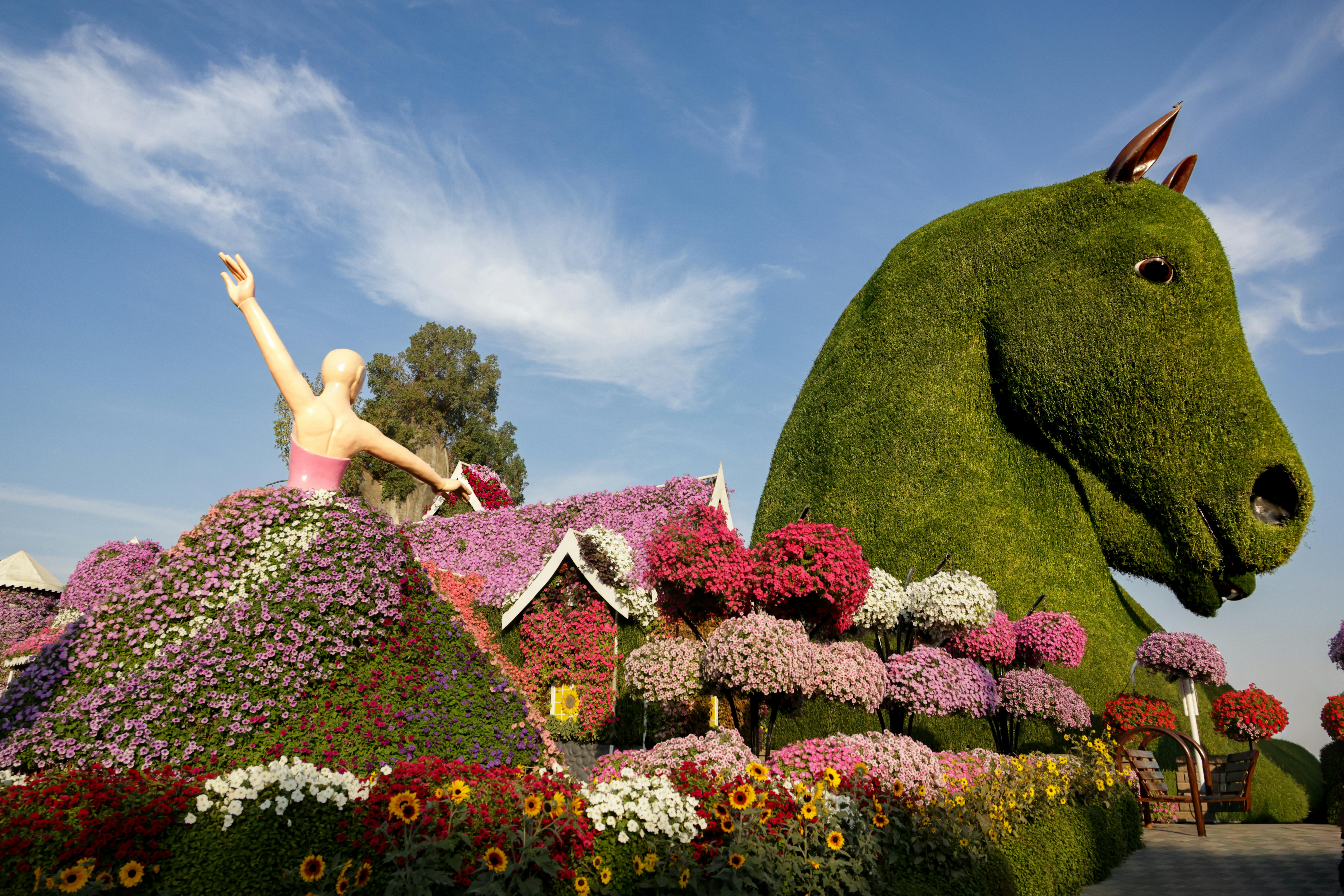 Vibrant garden featuring large floral sculptures of a horse and a dancer, under a clear blue sky.