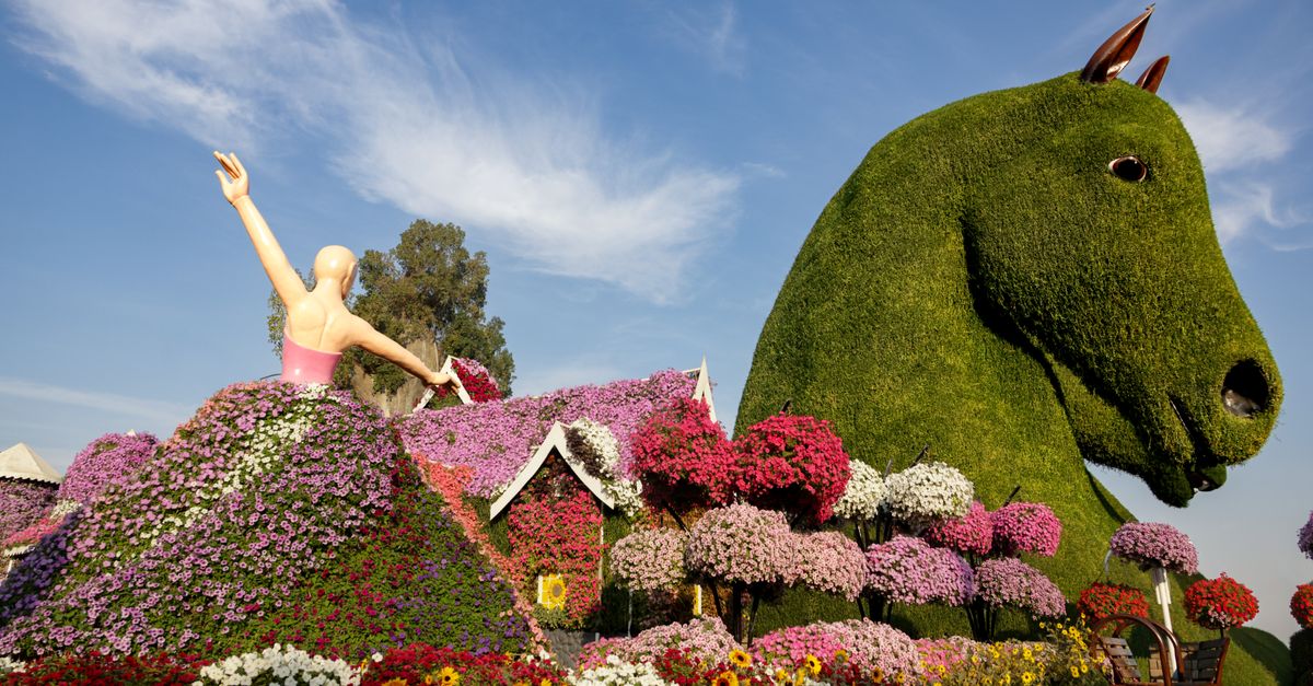 Vibrant garden featuring large floral sculptures of a horse and a dancer, under a clear blue sky.