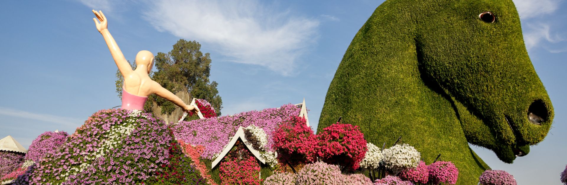 Vibrant garden featuring large floral sculptures of a horse and a dancer, under a clear blue sky.