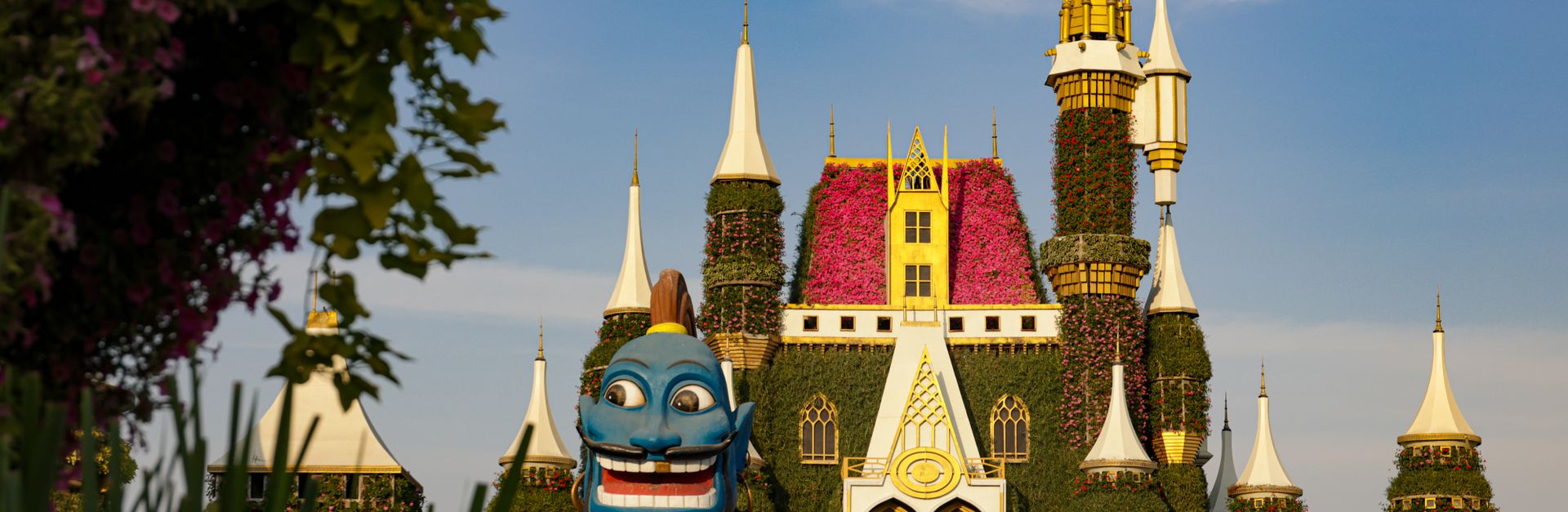 Enchanting garden castle with vibrant flowers and a whimsical blue genie statue under a clear blue s