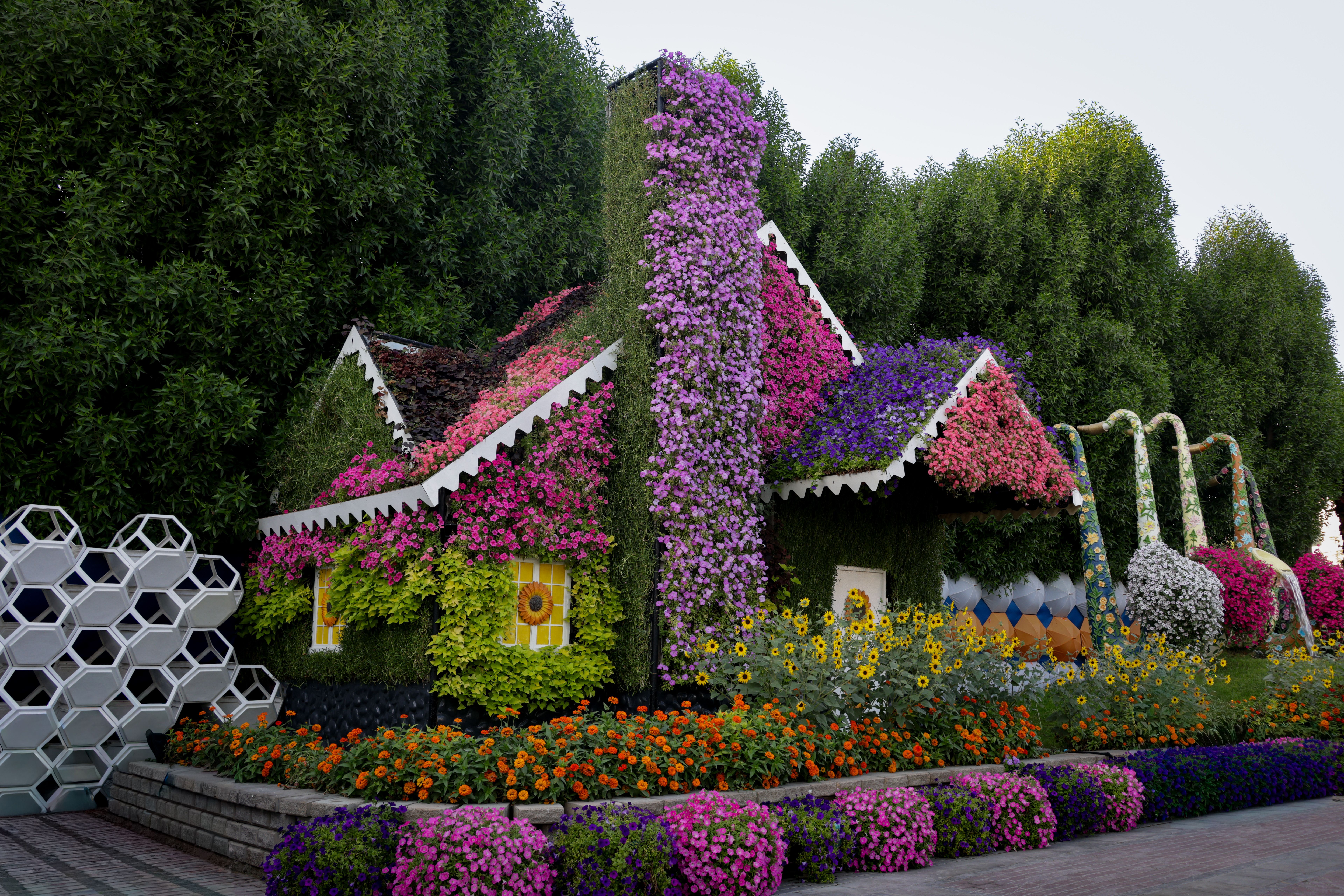 Charming cottage covered in colorful flowers, surrounded by lush greenery and vibrant flower beds.