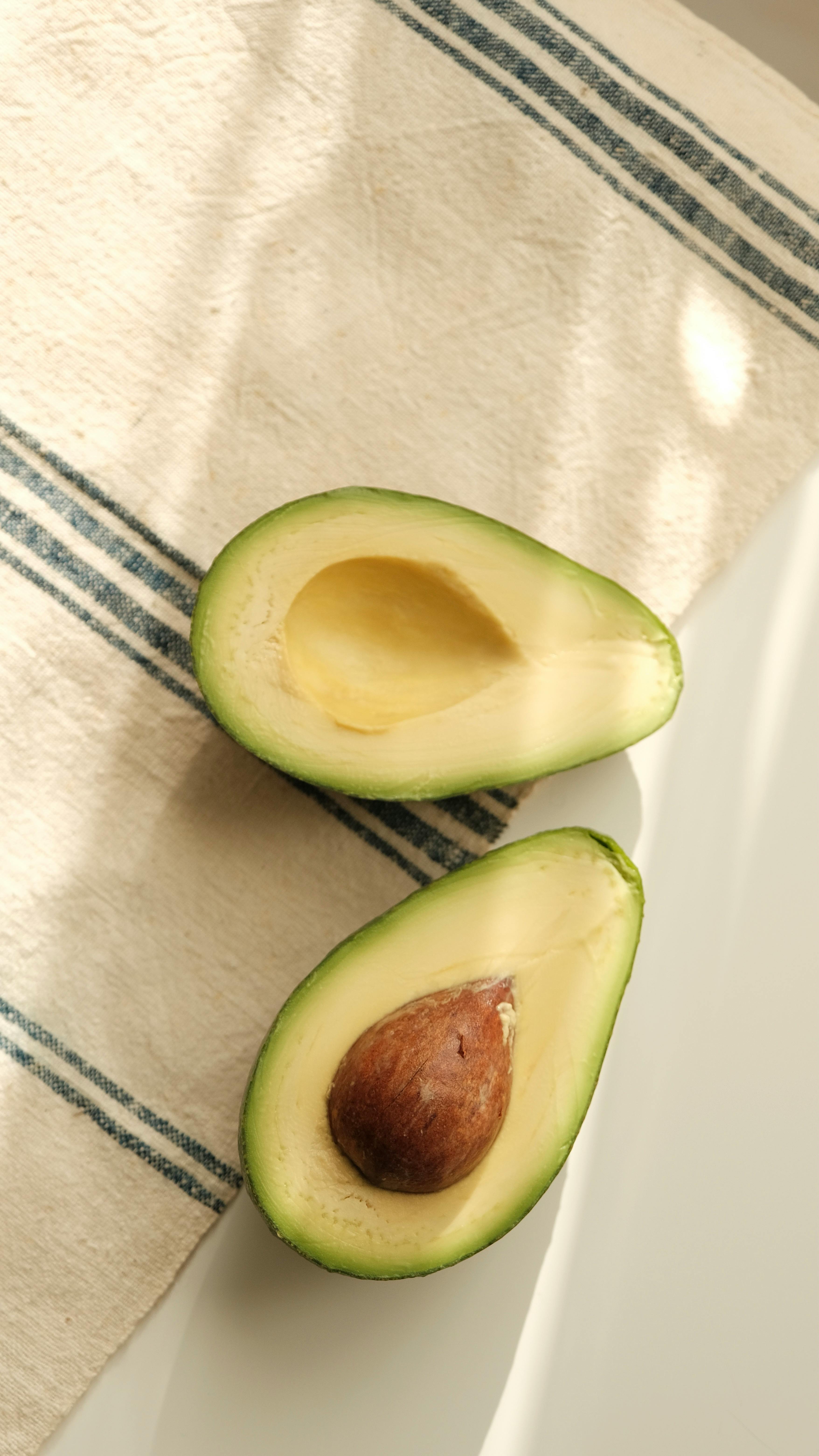 Top view of ripe avocado halves on striped kitchen cloth with natural lighting.