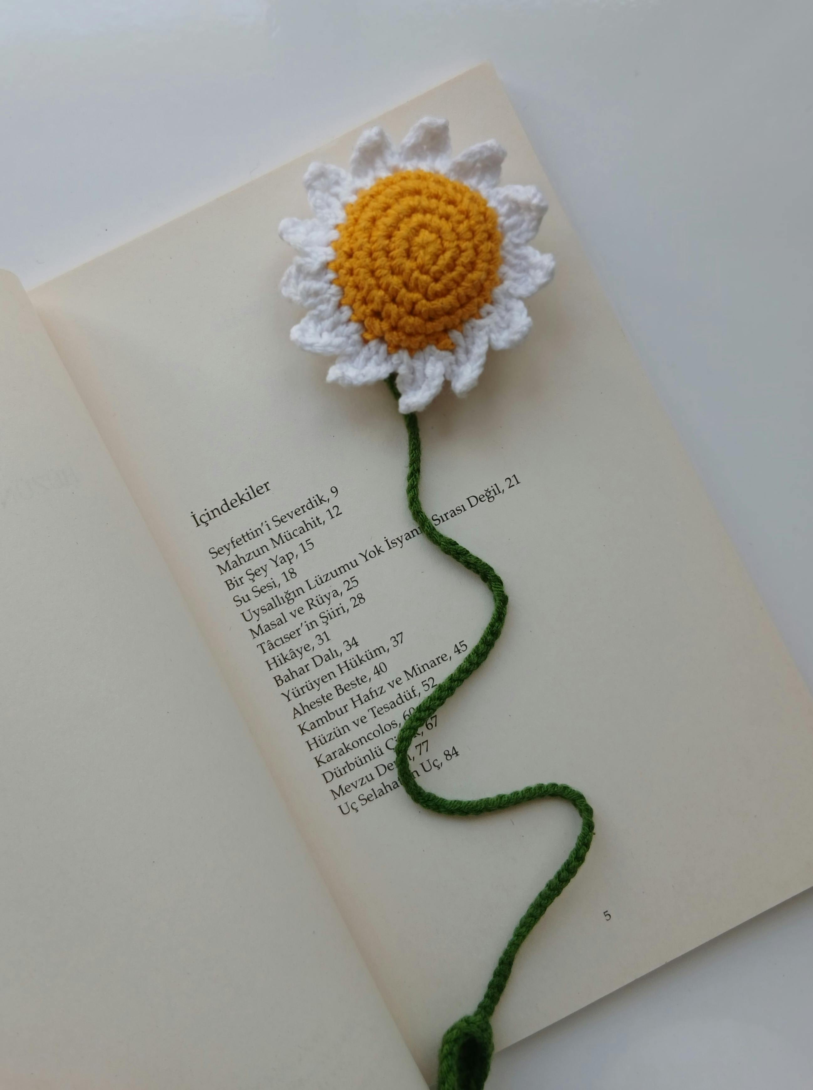 Bright crochet daisy bookmark with vibrant yellow and white petals on an open book.