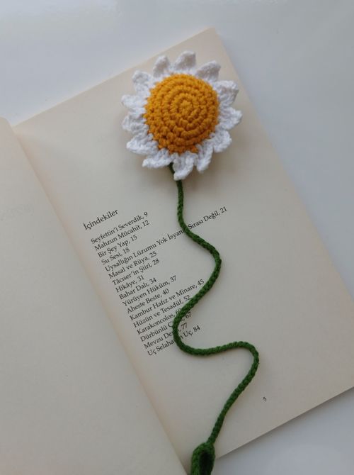 Free Bright crochet daisy bookmark with vibrant yellow and white petals on an open book. Stock Photo