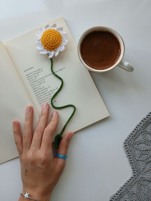 Free Hand reaching for crochet flower bookmark beside coffee and open book. Stock Photo