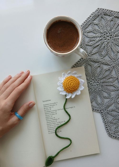 Free Hand resting on book with coffee cup and crochet flower bookmark on a lace mat. Stock Photo