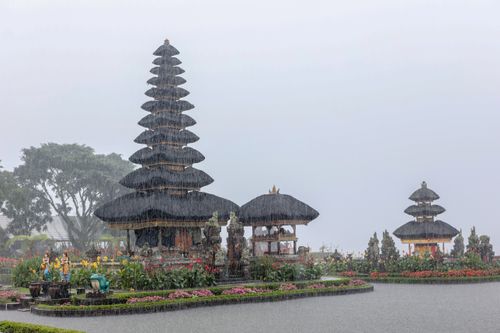 Free Scenic view of Ulun Danu Beratan Temple surrounded by lush greenery and vibrant flowers in the rain. Stock Photo