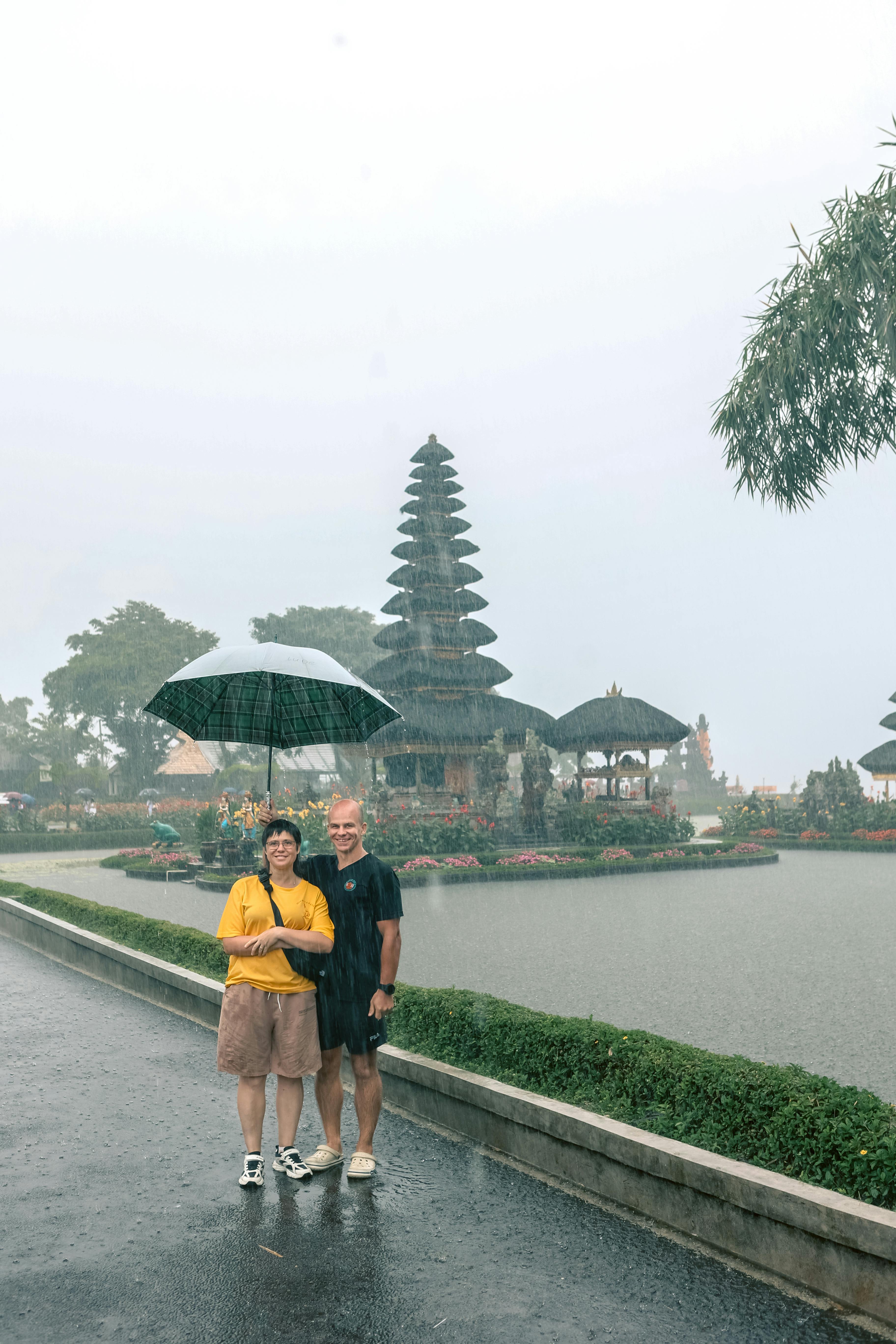 A couple stands under an umbrella in the rain at Ulun Danu Beratan Temple, Bali, Indonesia.