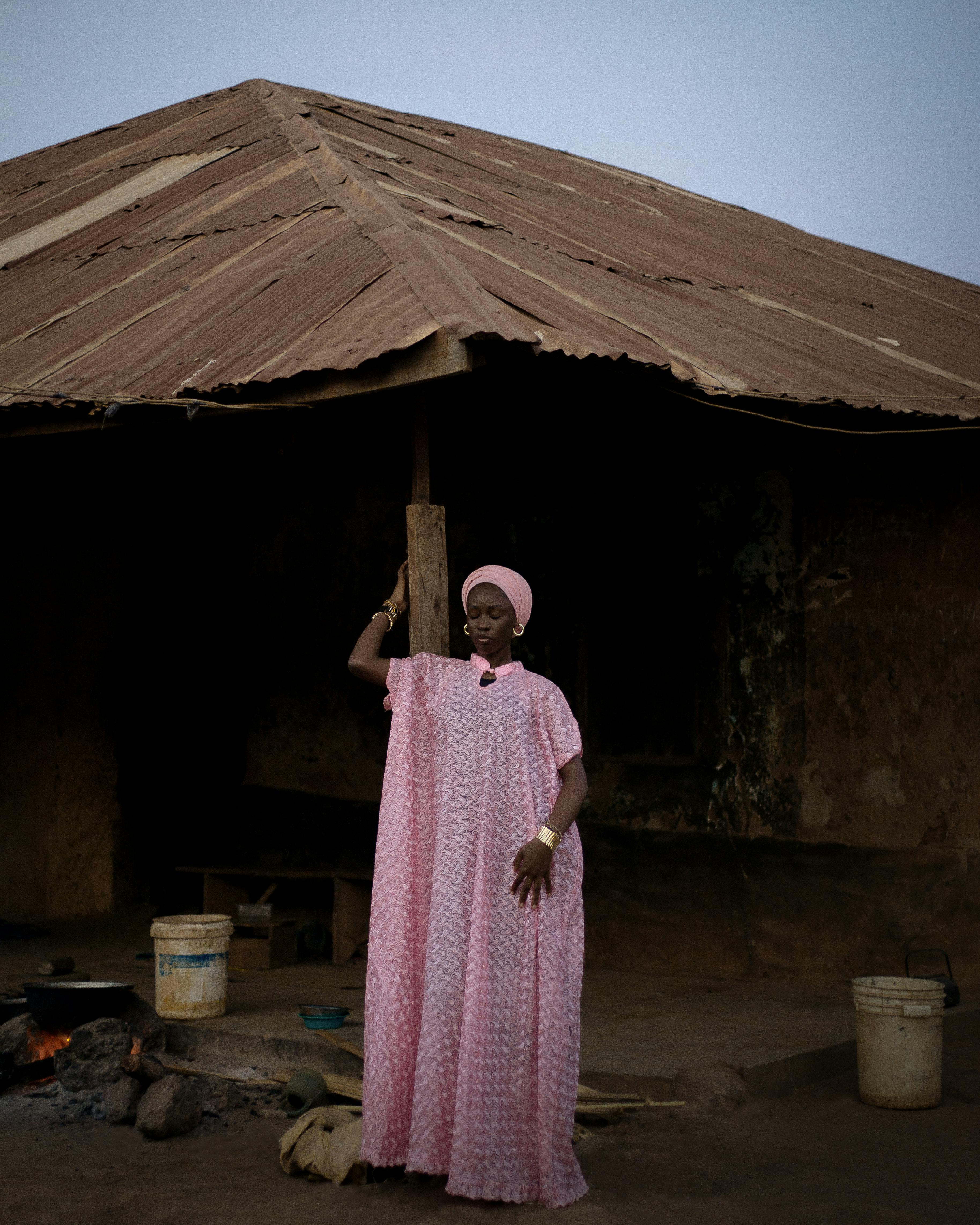 A woman in traditional attire poses in front of a rustic house in Ilorin, Nigeria.