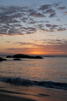 Peaceful sunset over ocean with rocks and gentle waves.