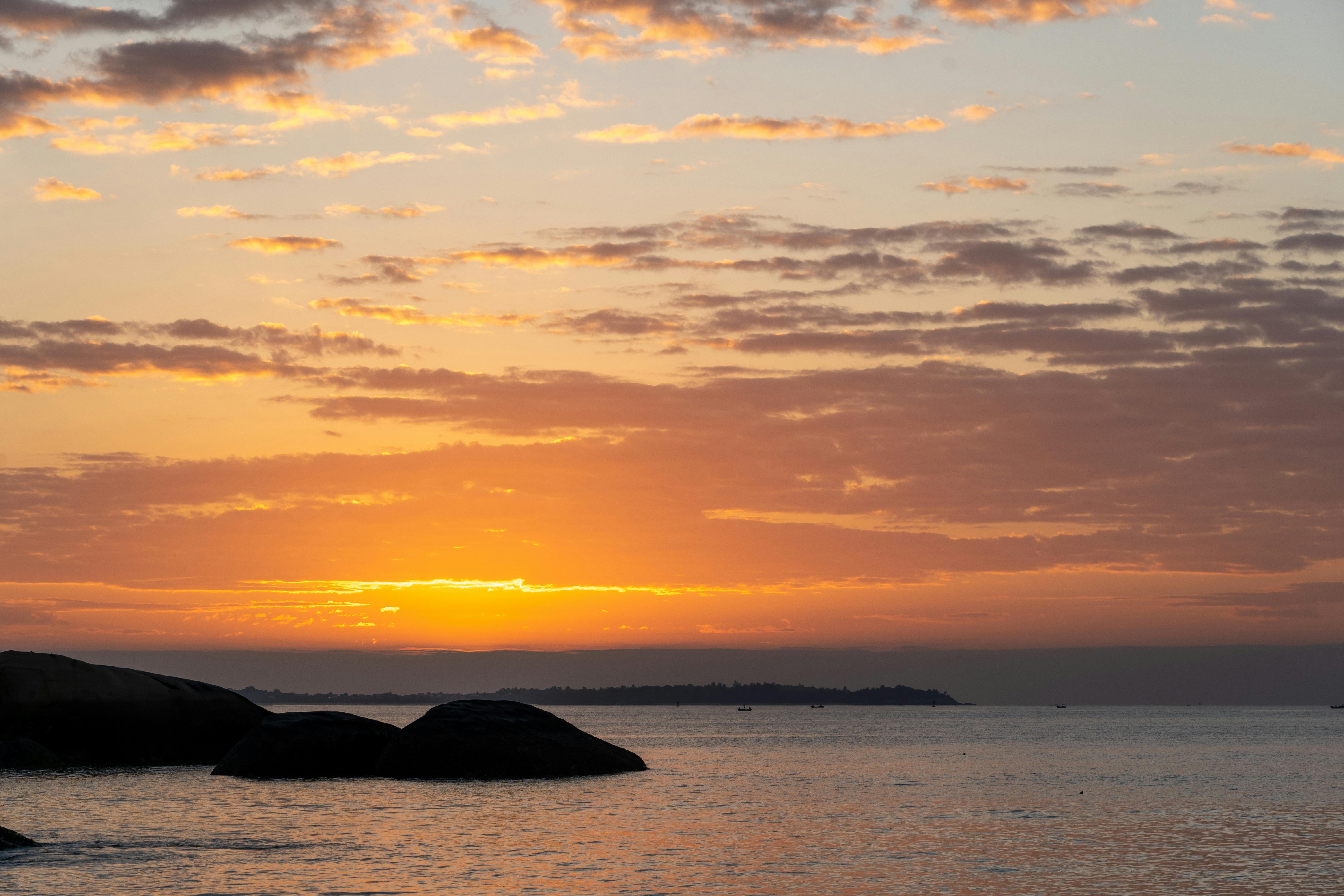 A serene sunset over the ocean with silhouetted rocks in the foreground, creating a peaceful ambiance.