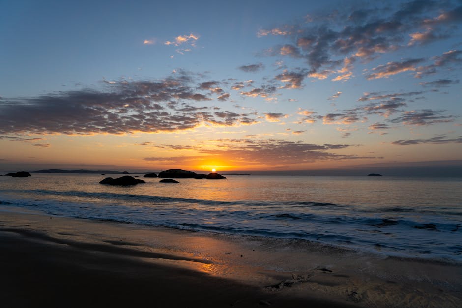 Peaceful sunset over a tranquil beach with dramatic clouds and calm sea waves.