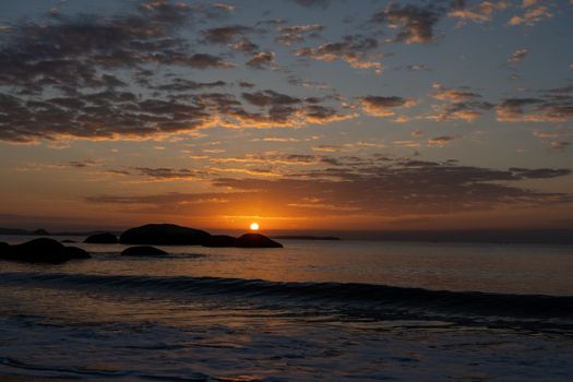 Peaceful sunrise over the ocean with silhouette of rocks and vibrant sky.
