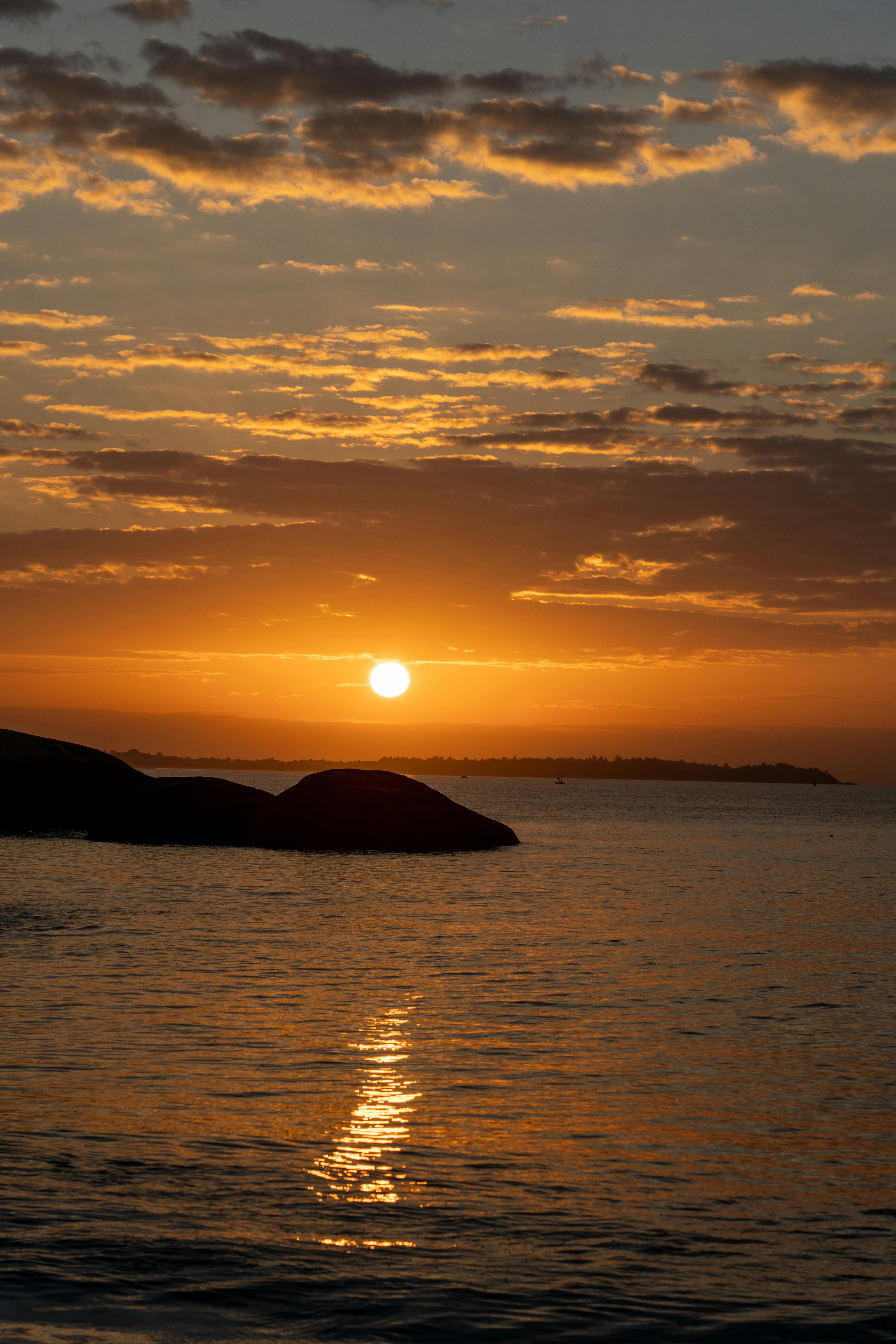 Gratis Un tramonto incantevole sull'oceano con vivaci tonalità arancioni e rocce in silhouette. Foto a disposizione