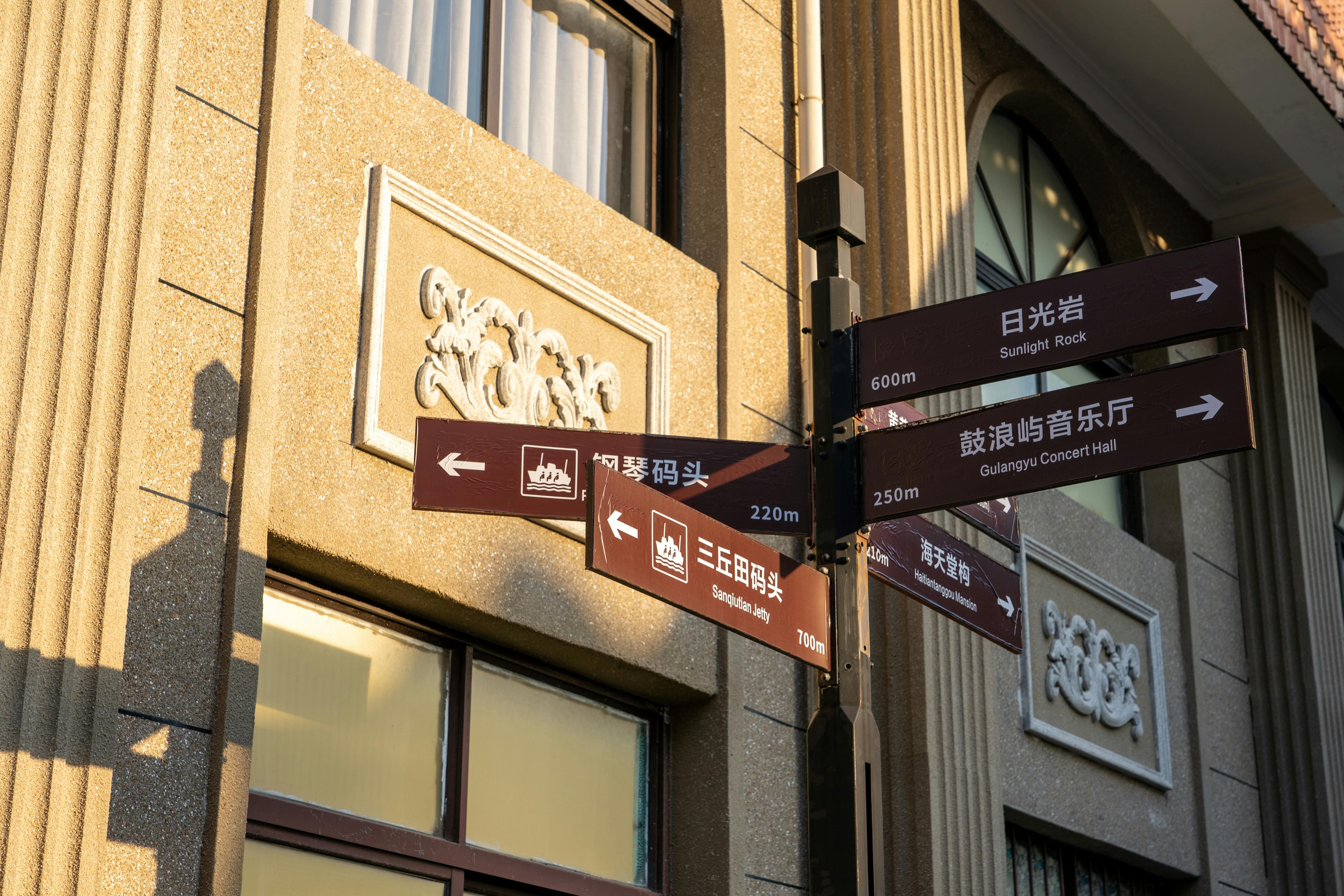 Street signposts guide tourists to notable Gulangyu Island attractions under soft sunlight.