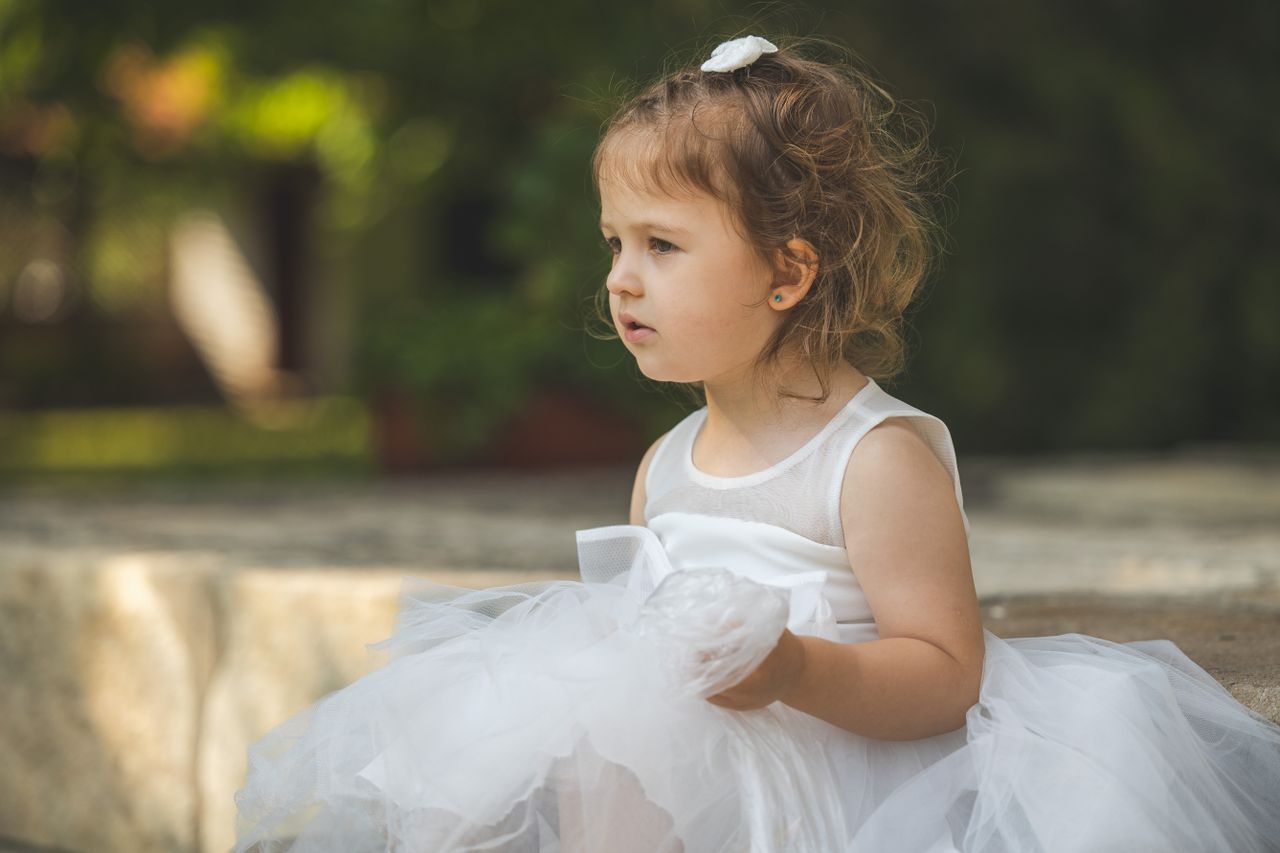 a young girl in a white dress sits outdoors enjoying a sunny day