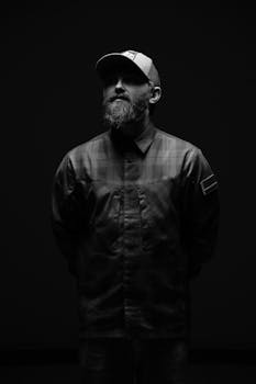 A dramatic black and white portrait of a bearded man in a cap.