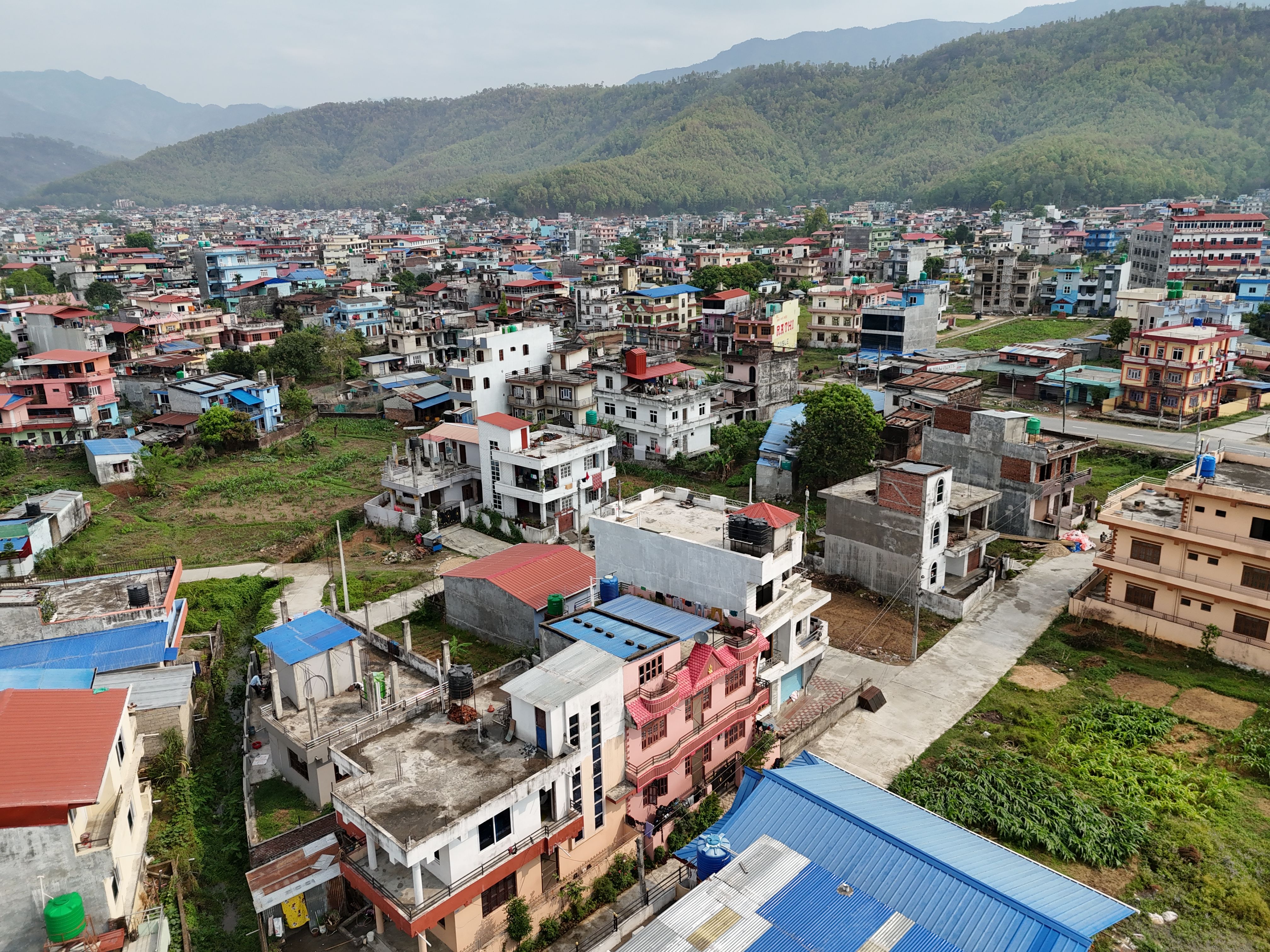 Aerial view showcasing a dense, colorful urban neighborhood nestled between lush green hills in Nepal.