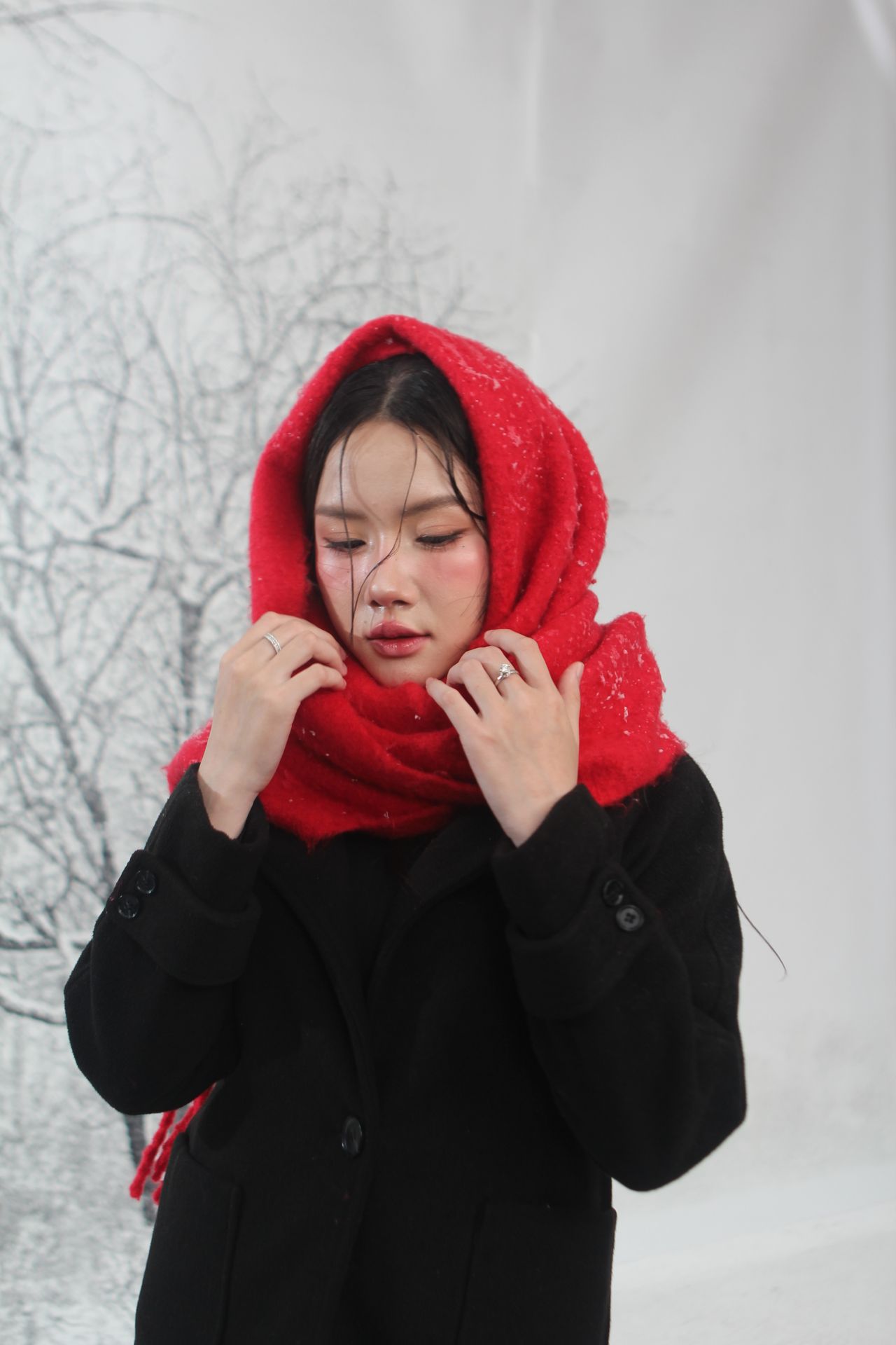 Woman with a red scarf pulled up as a hood over a black coat