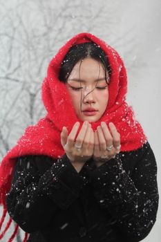 Woman with red scarf enjoying snowfall, serene winter scene.