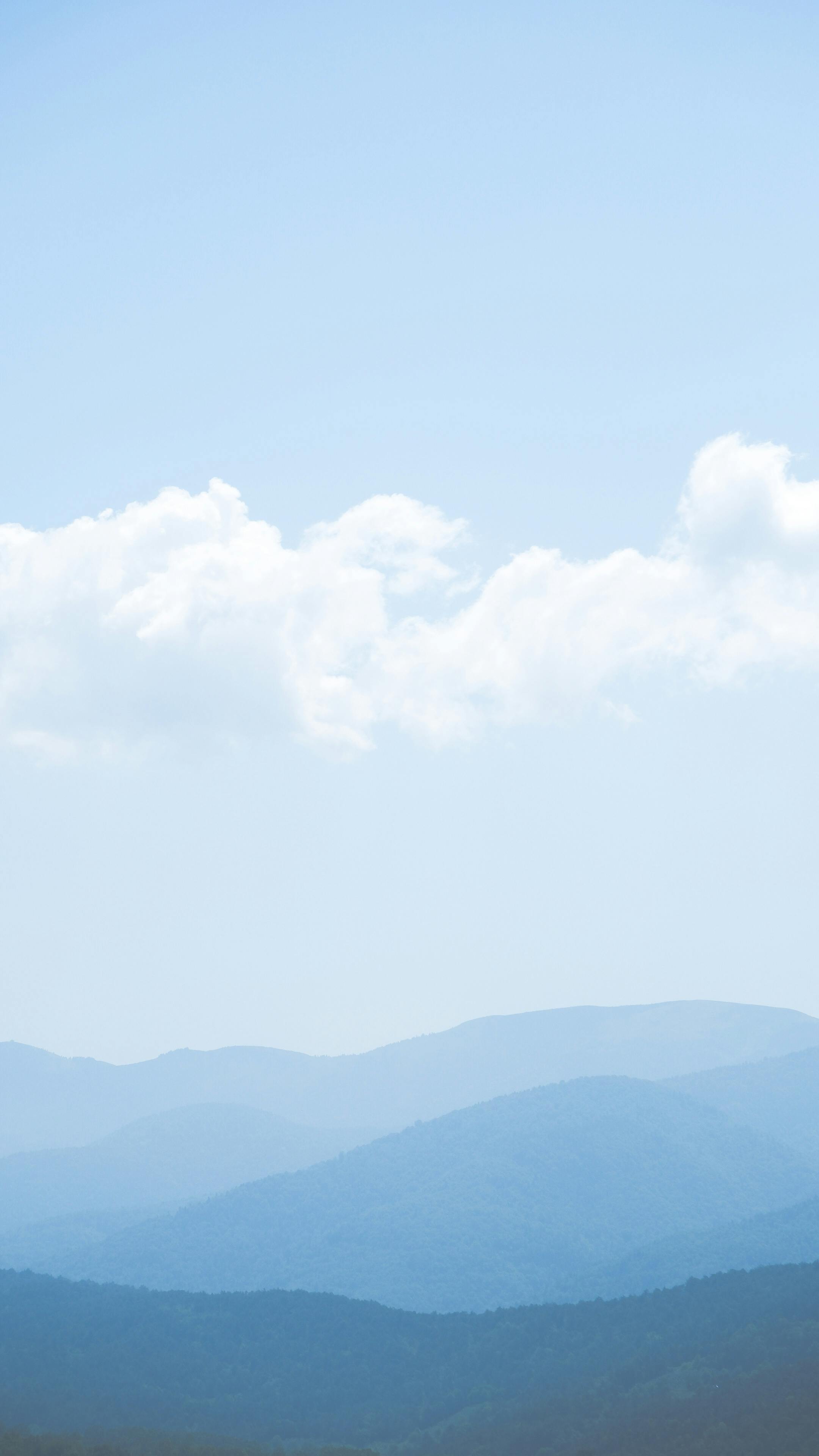 Layered blue mountains under fluffy clouds, creating a calming scenic view.