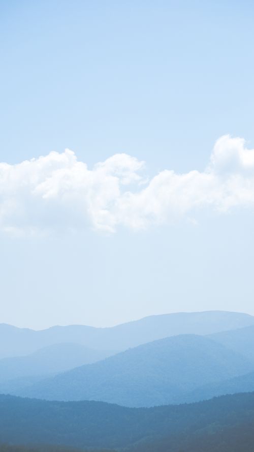 Free Layered blue mountains under fluffy clouds, creating a calming scenic view. Stock Photo