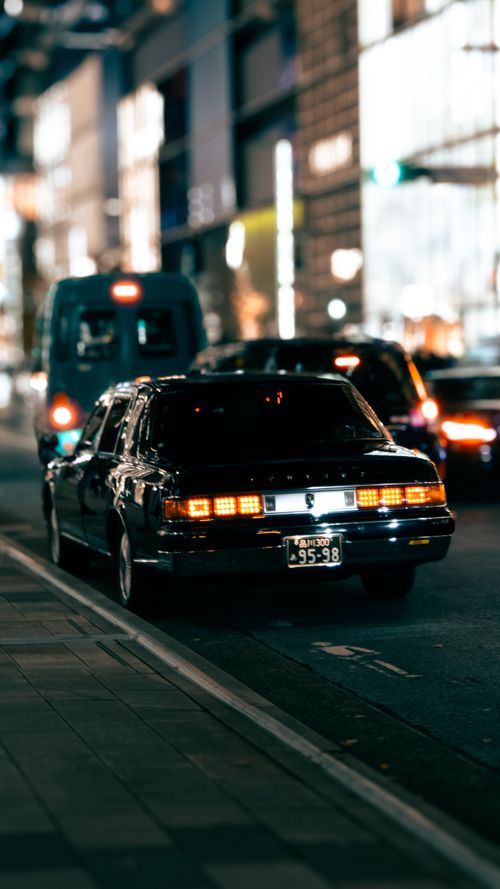 Free A vintage car on a vibrant city street at night, showcasing urban life and motion. Stock Photo