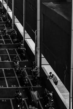 Monochrome image of a parking area with scooters and a person, viewed from above, conveying an urban feel.