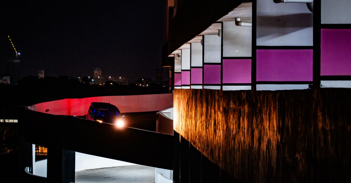 Car on a curved ramp in a parking structure at night, with city lights in the background.