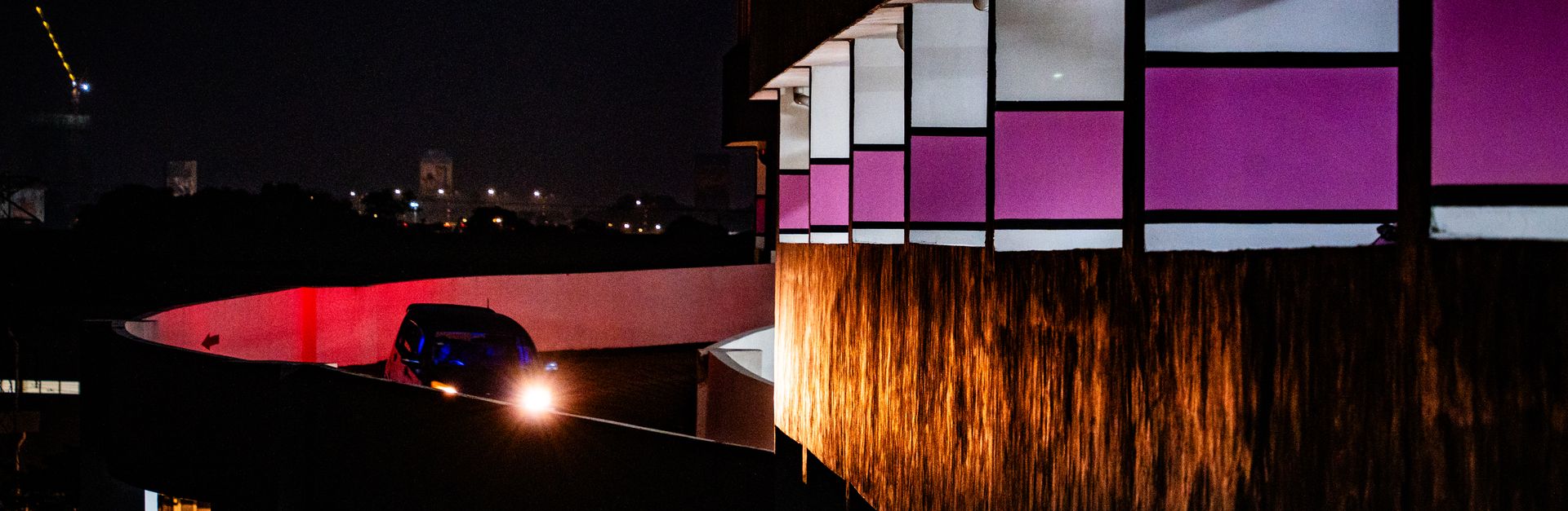 Car on a curved ramp in a parking structure at night, with city lights in the background.