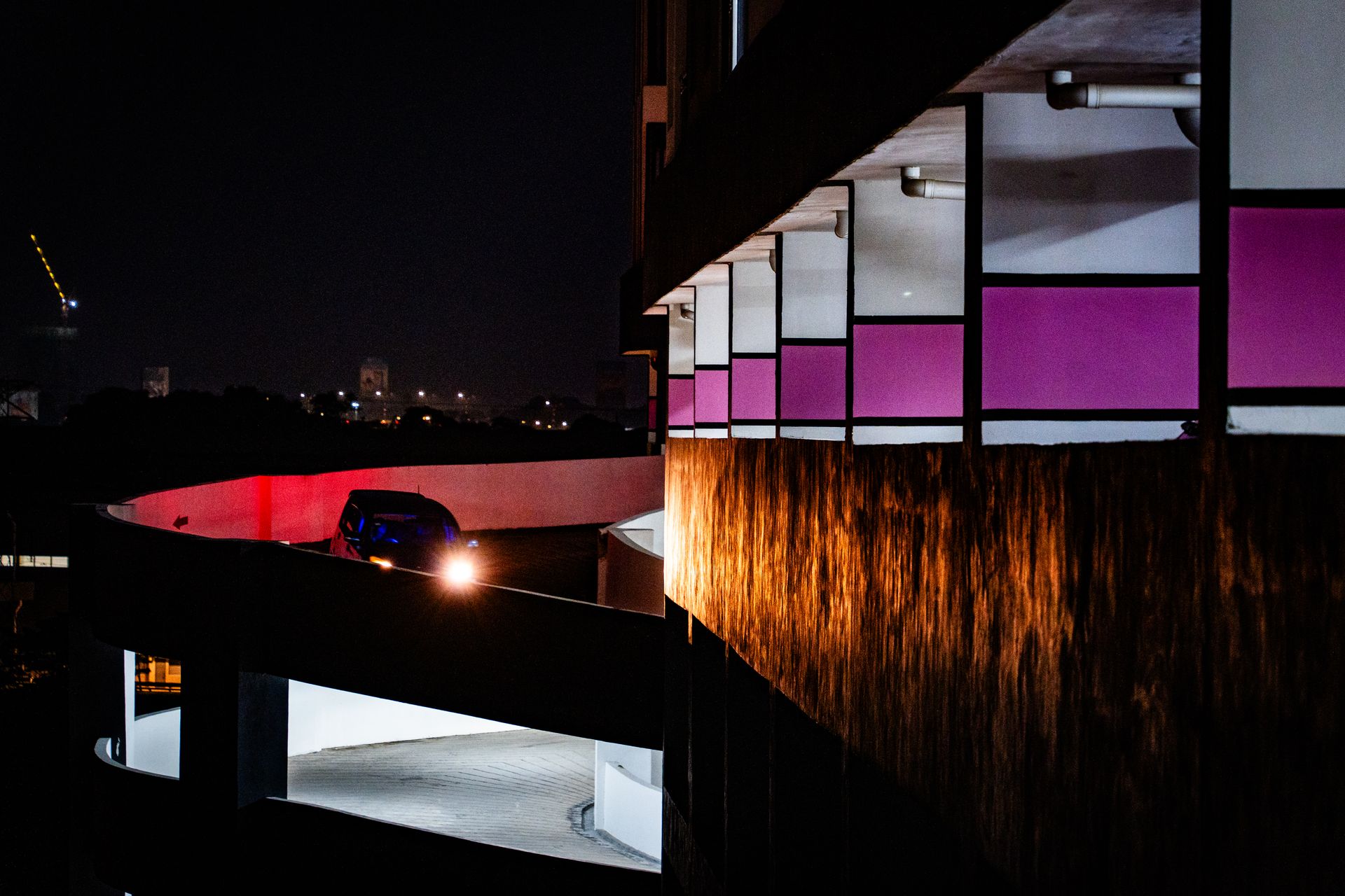 Car on a curved ramp in a parking structure at night, with city lights in the background.