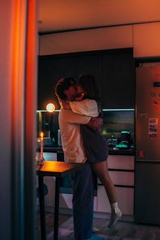 A couple sharing a romantic moment in a cozy, dimly lit kitchen setting.