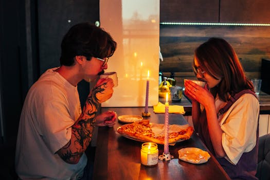 A couple enjoys a cozy candlelit dinner with pizza and drinks, creating a warm, romantic atmosphere.