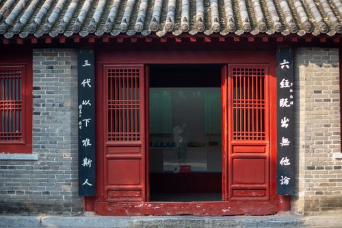 Free A facade of traditional Chinese architecture featuring a red door and cultural calligraphy on the wall. Stock Photo