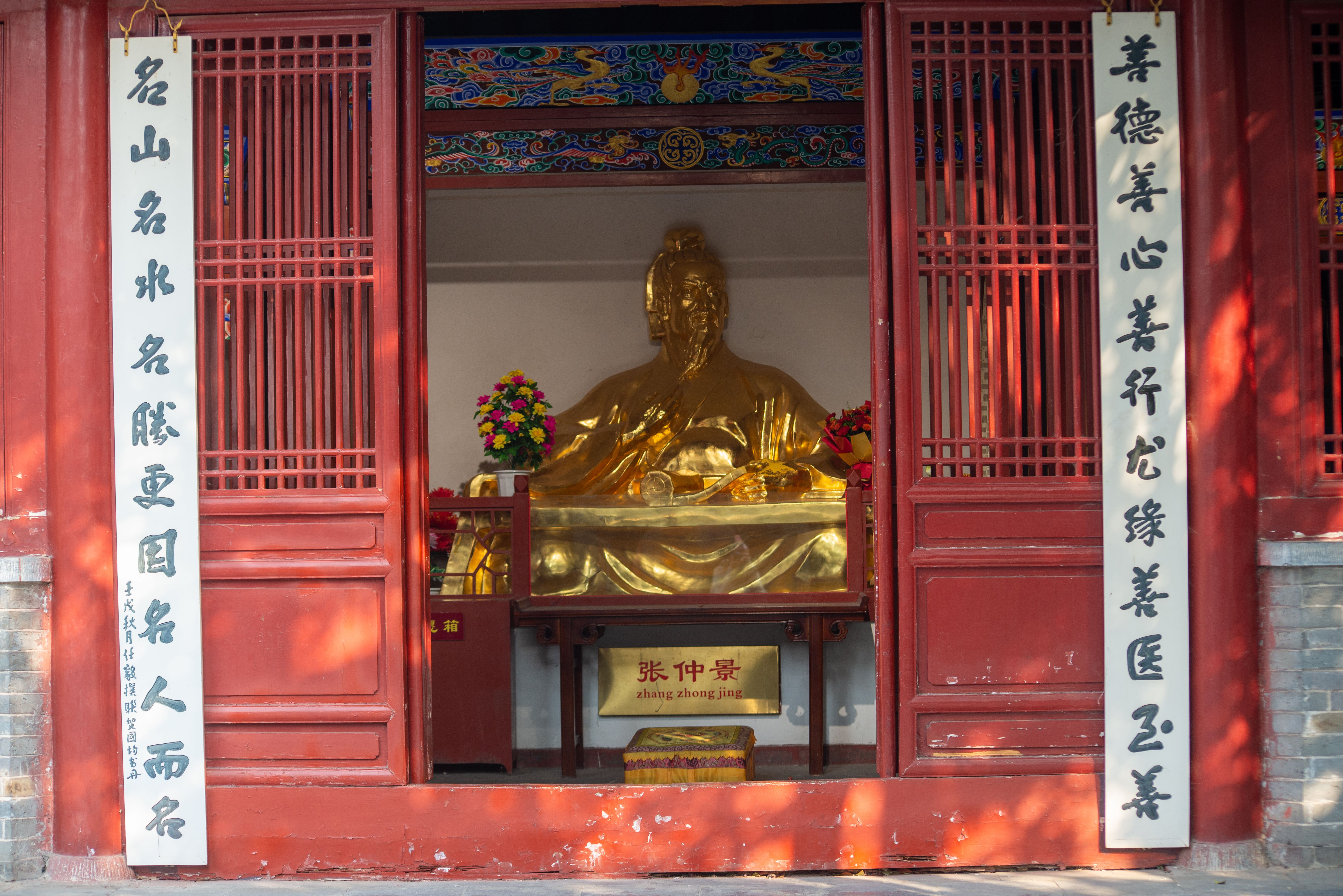 Golden statue inside Chinese temple with red wooden doors and traditional decorations.