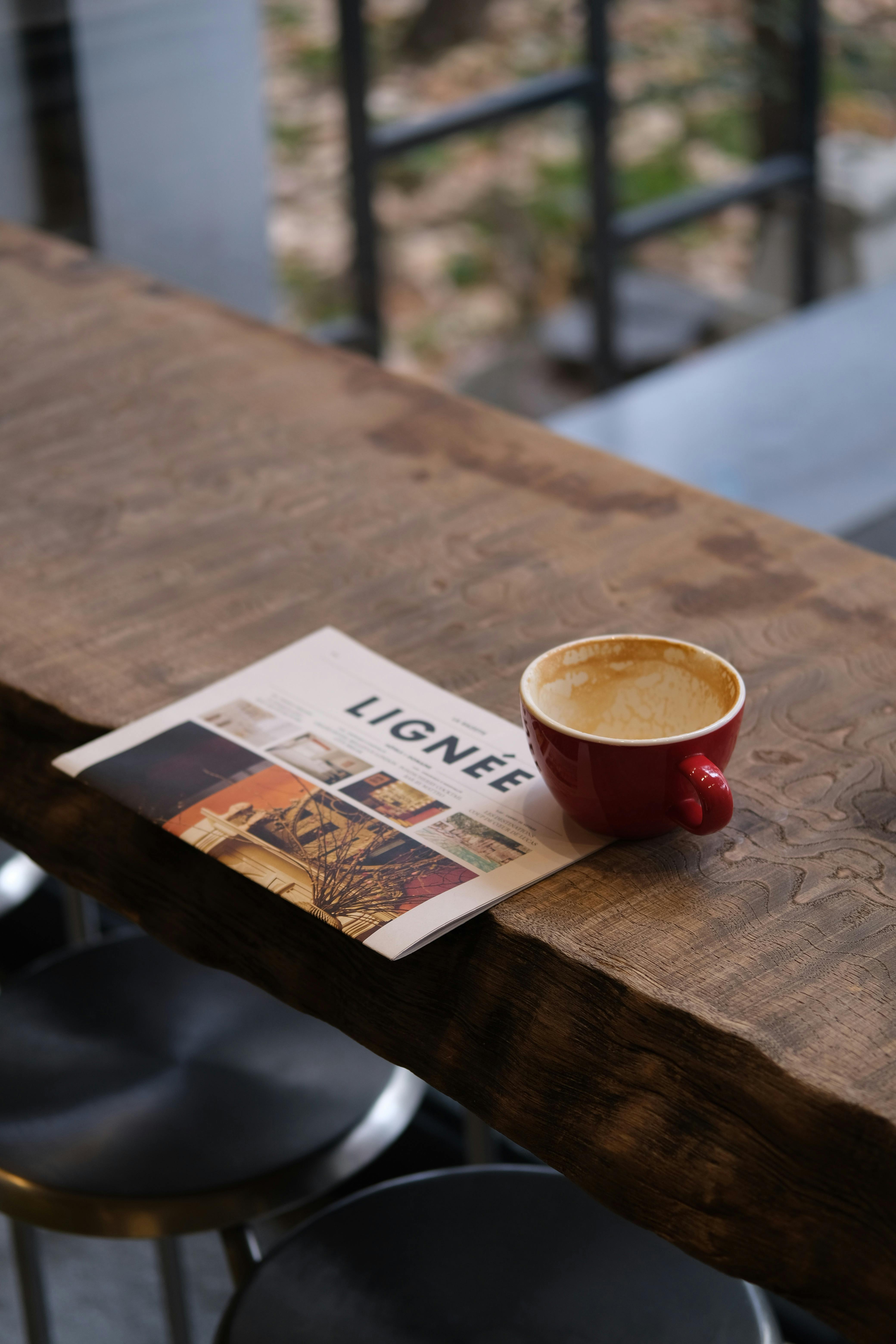 A red coffee cup and magazine on a rustic wooden table create a cozy setting.