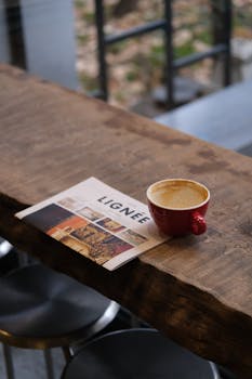 A red coffee cup and magazine on a rustic wooden table create a cozy setting.