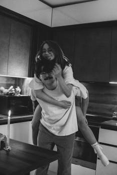 A joyful couple shares a playful moment indoors, enhancing warmth and intimacy in their modern kitchen.