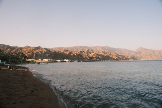 Tranquil beach scene with mountains and calm waters at sunset, ideal for relaxation themes.