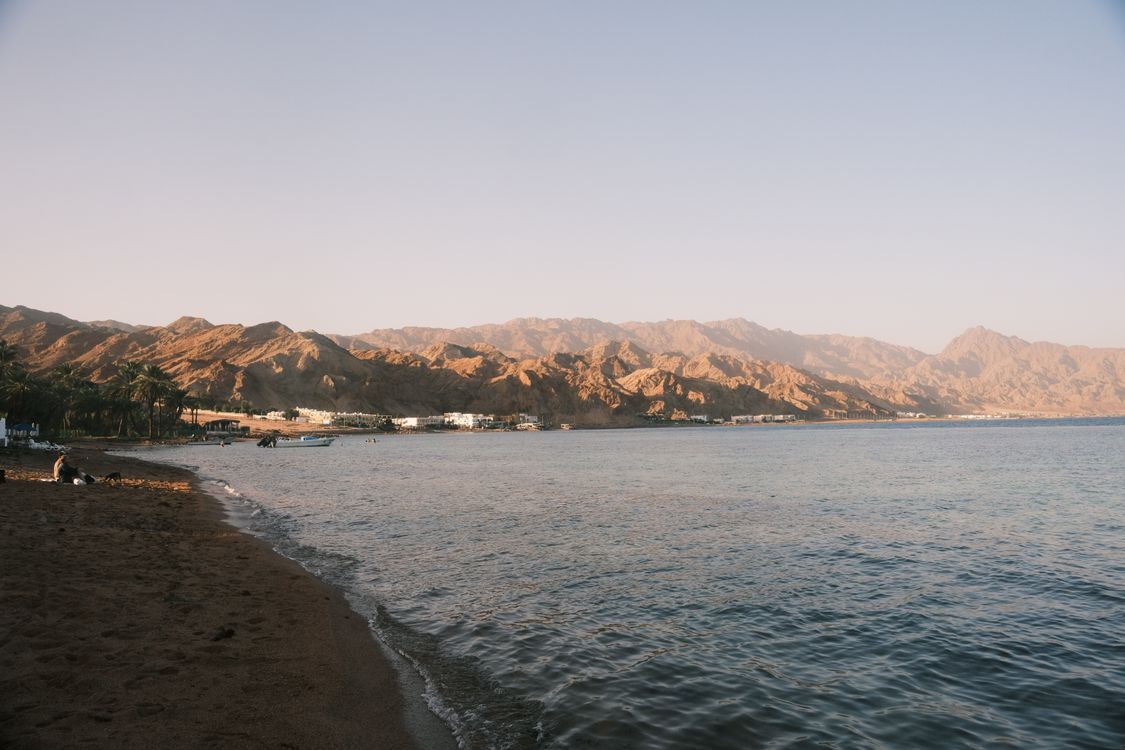 Free Tranquil beach scene with mountains and calm waters at sunset, ideal for relaxation themes. Stock Photo
