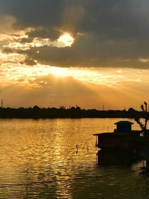 Free Sunset reflecting golden hues on a serene river with silhouetted structures. Stock Photo